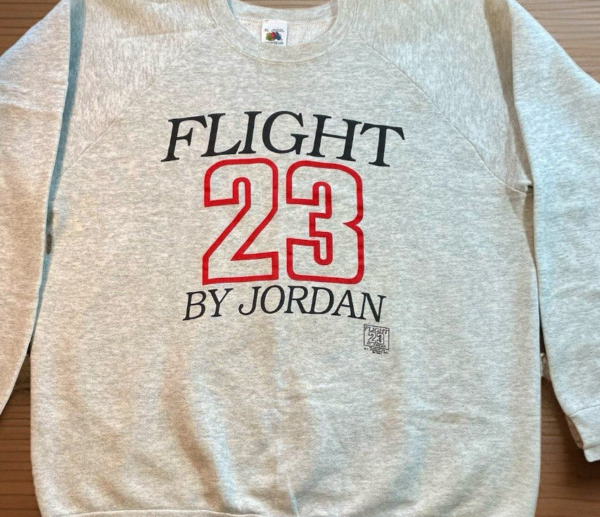 Beige sweatshirt with 'FLIGHT 23 BY JORDAN' text on a wooden surface
