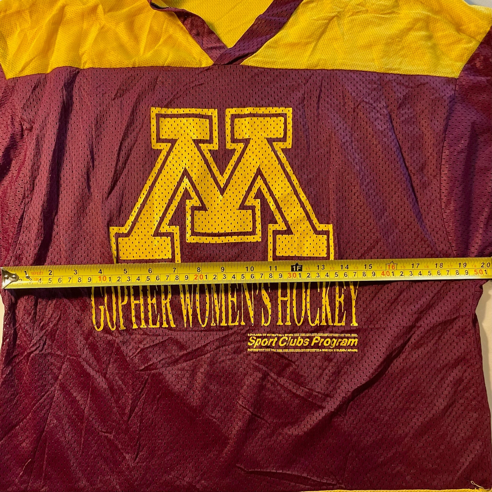Maroon and yellow sports jacket with a logo and text, measured by a tape measure.