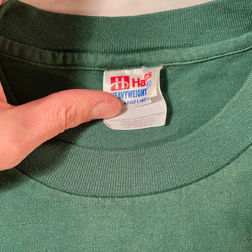 Hand holding a label on a green shirt with visible text and logos.