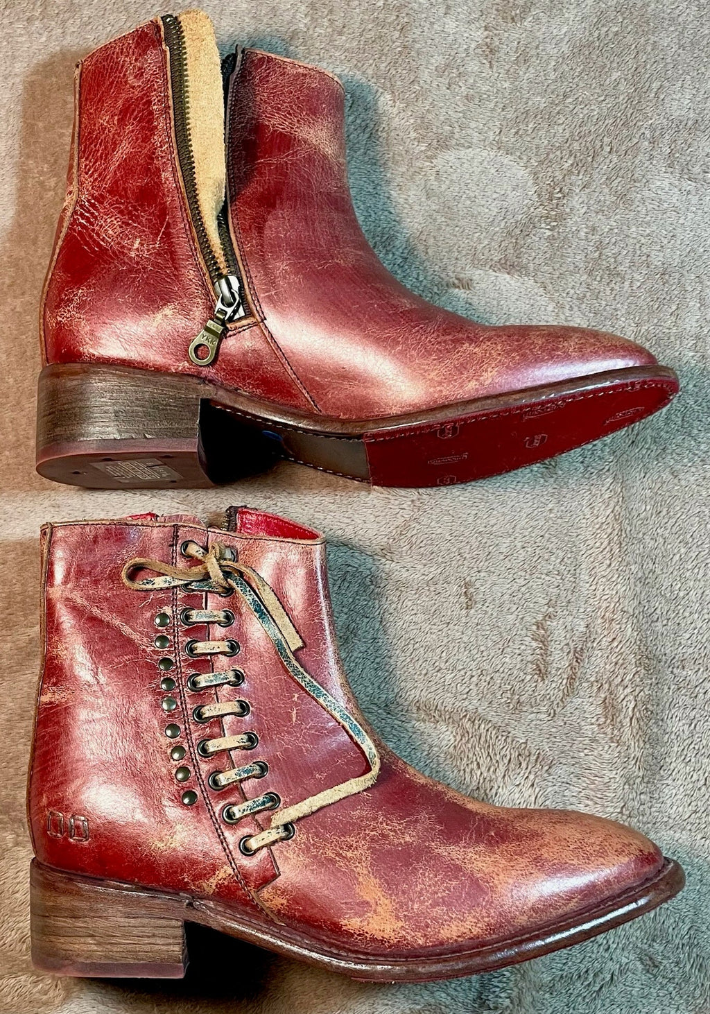 Pair of red leather boots with gold zippers on a textured surface