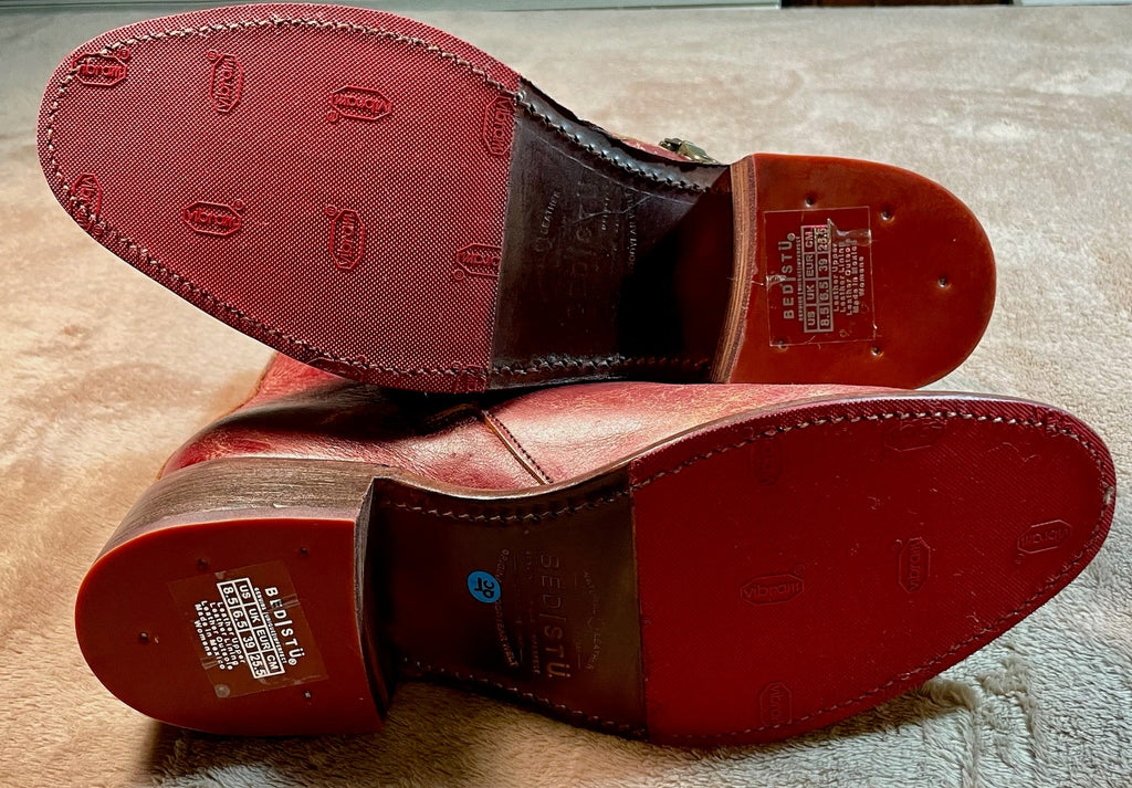 Brown leather shoes with red soles on a textured surface