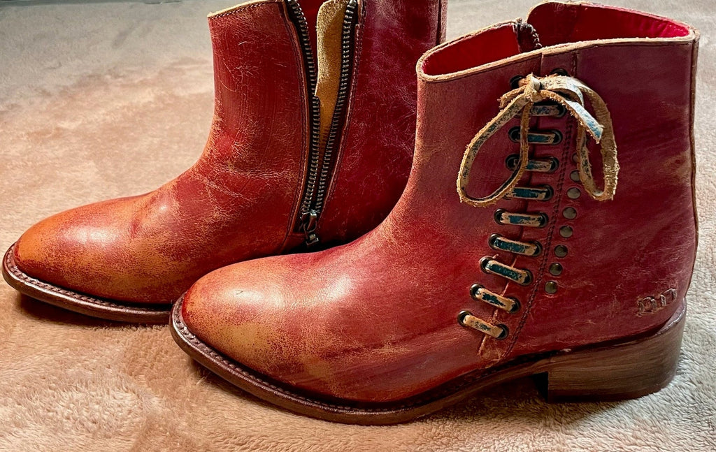 Pair of red leather boots with laces and a zipper on a textured surface.