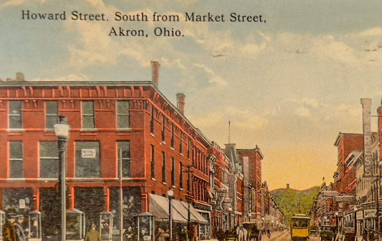 Vintage street scene of Howard Street in Akron, Ohio, with red brick buildings and a yellow trolley.