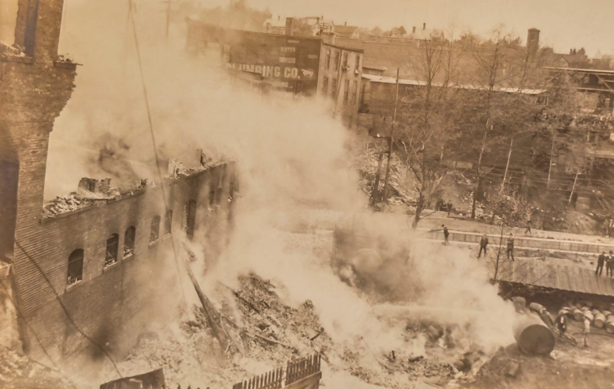 A sepia-toned photograph of a destroyed urban area with smoke billowing from buildings.
