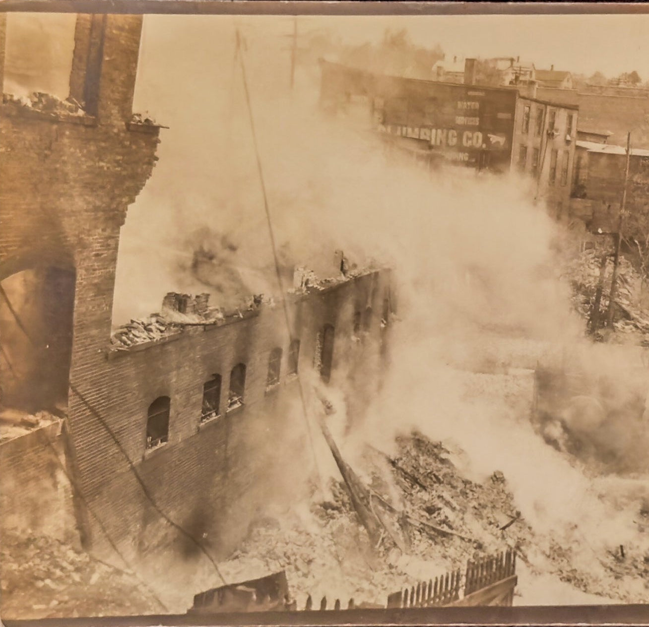 A sepia-toned photograph of a destroyed urban area with smoke billowing from buildings.