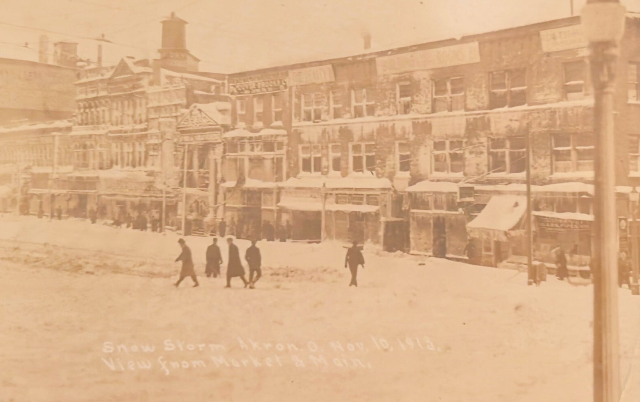 Vintage sepia-toned photograph of a snowy street scene with people and buildings.