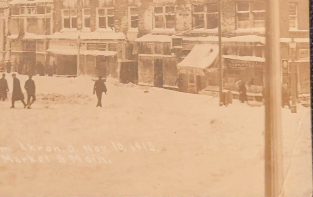 Vintage sepia-toned photograph of a snowy street scene with people and buildings.