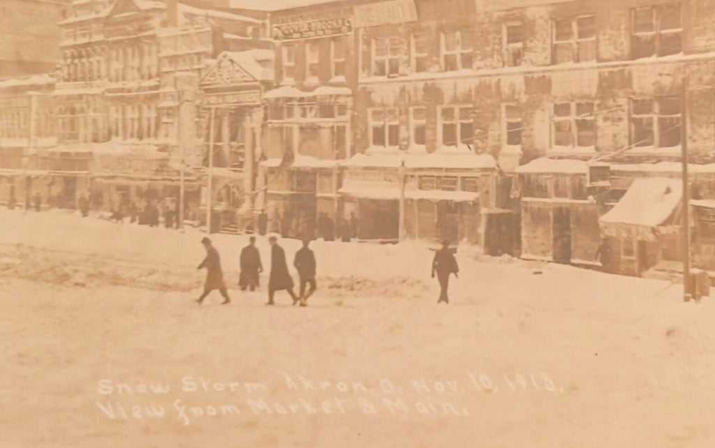Vintage sepia-toned photograph of a snowy street scene with people and buildings.