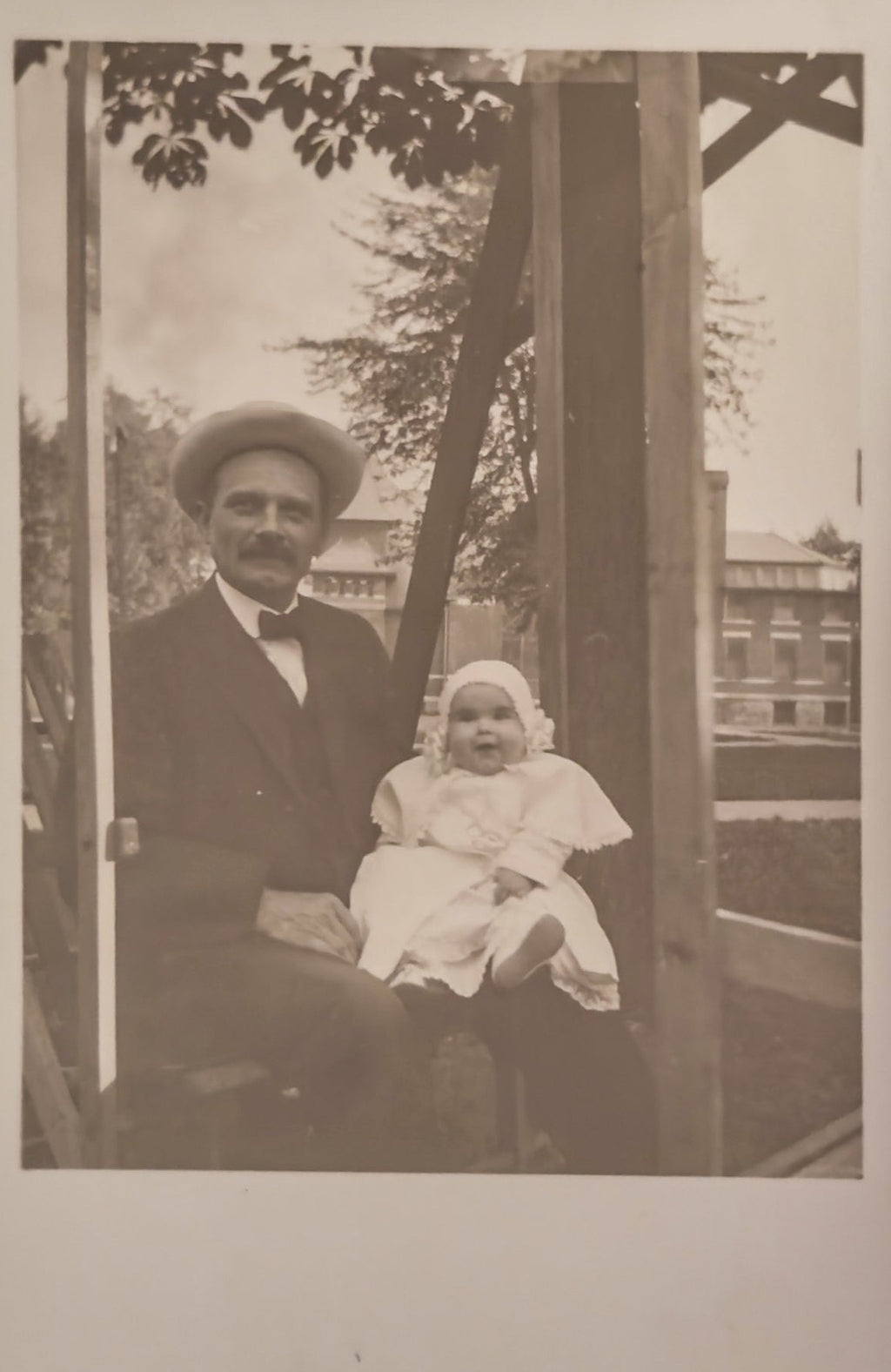 Vintage black and white photo of a man and a baby sitting together outdoors.
