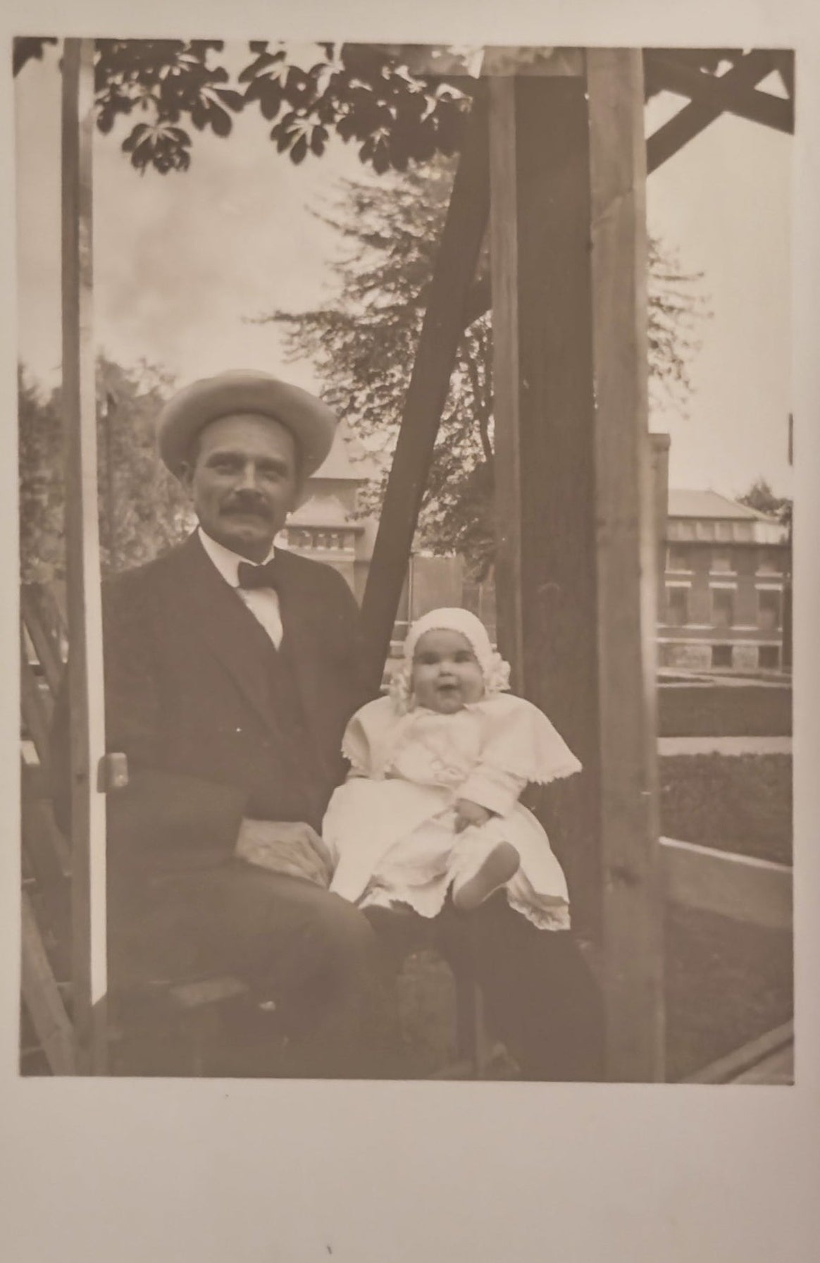 Vintage black and white photo of a man and a baby sitting together outdoors.