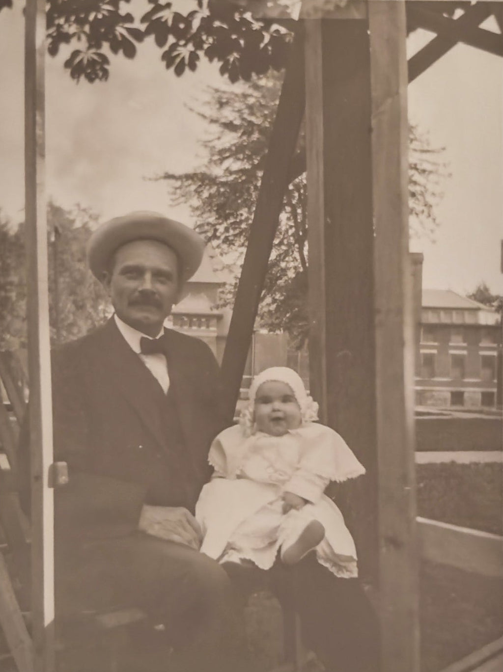 Vintage black and white photo of a man and a baby sitting together outdoors.
