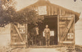Vintage sepia-toned photograph of a man standing in front of a wooden shed with a horse inside.