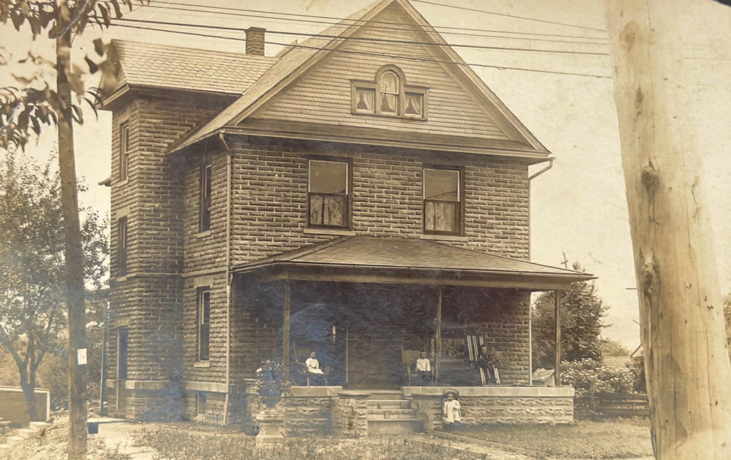 Vintage black and white photo of a two-story house with a porch.