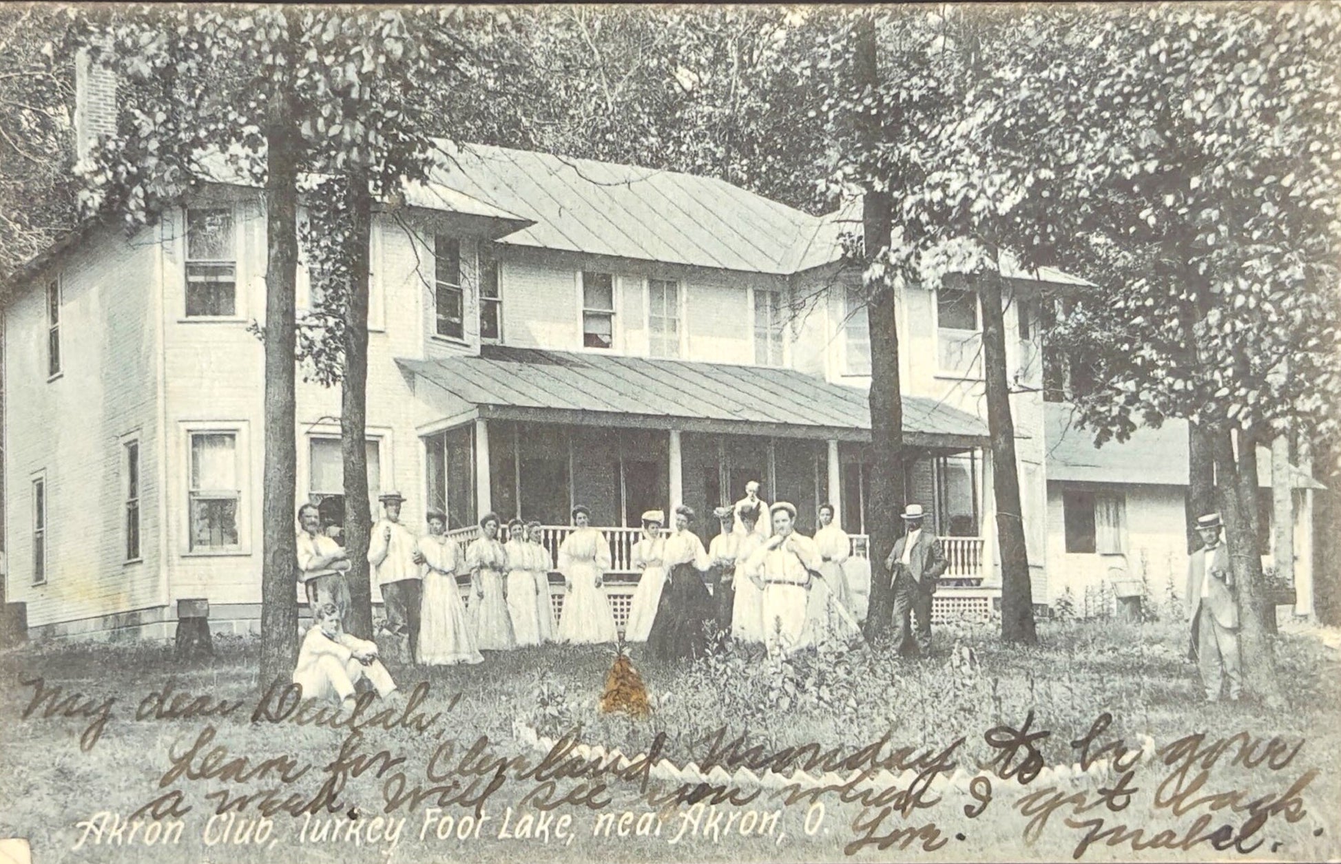 Vintage photograph of a group of people standing outside a house with trees in the background.