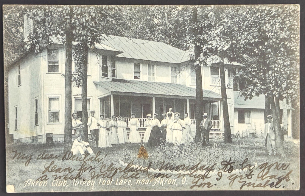 Vintage photograph of a group of people standing on a porch in front of a house with trees and a garden.