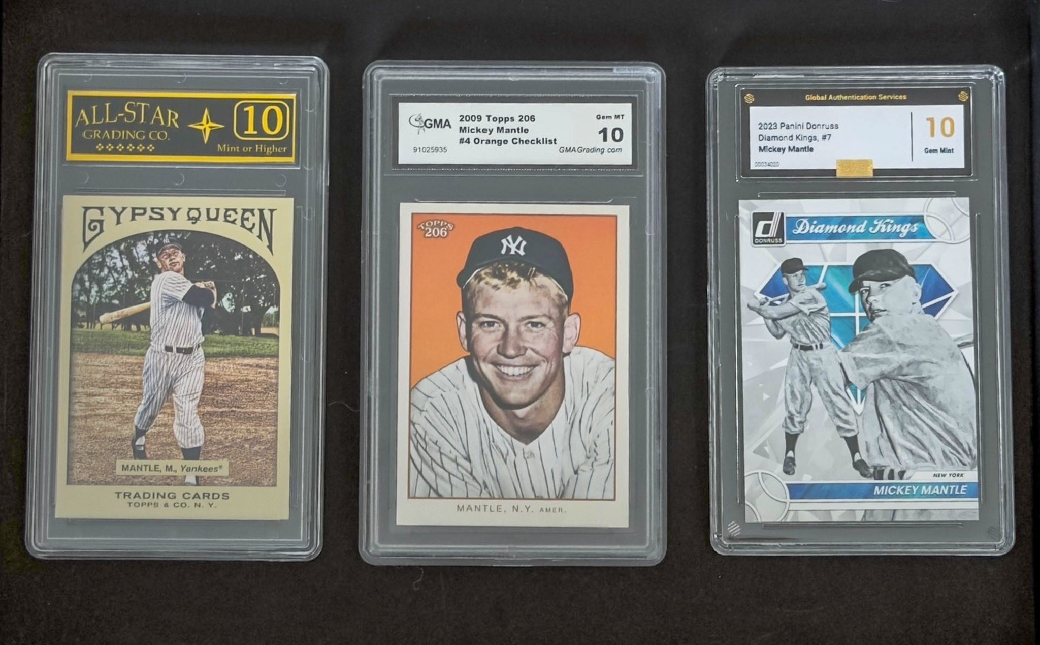 Three baseball trading cards in protective cases on a dark background