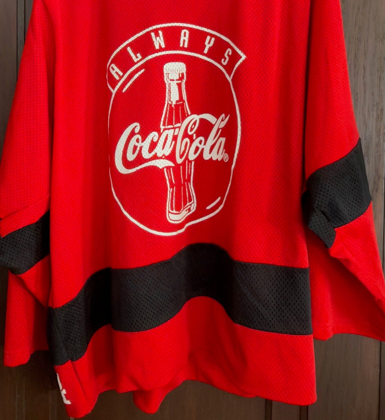 Red jersey with Coca-Cola logo on a hanger against a wooden door.
