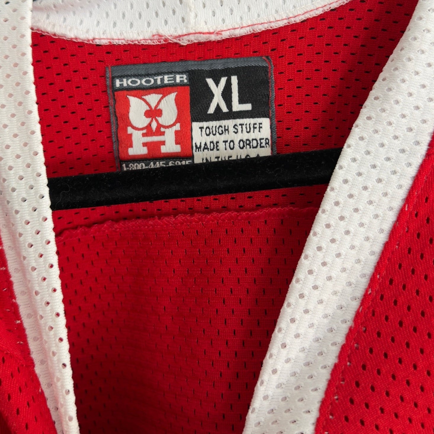 Red and white mesh jersey with Hooters logo and XL tag on a wooden surface