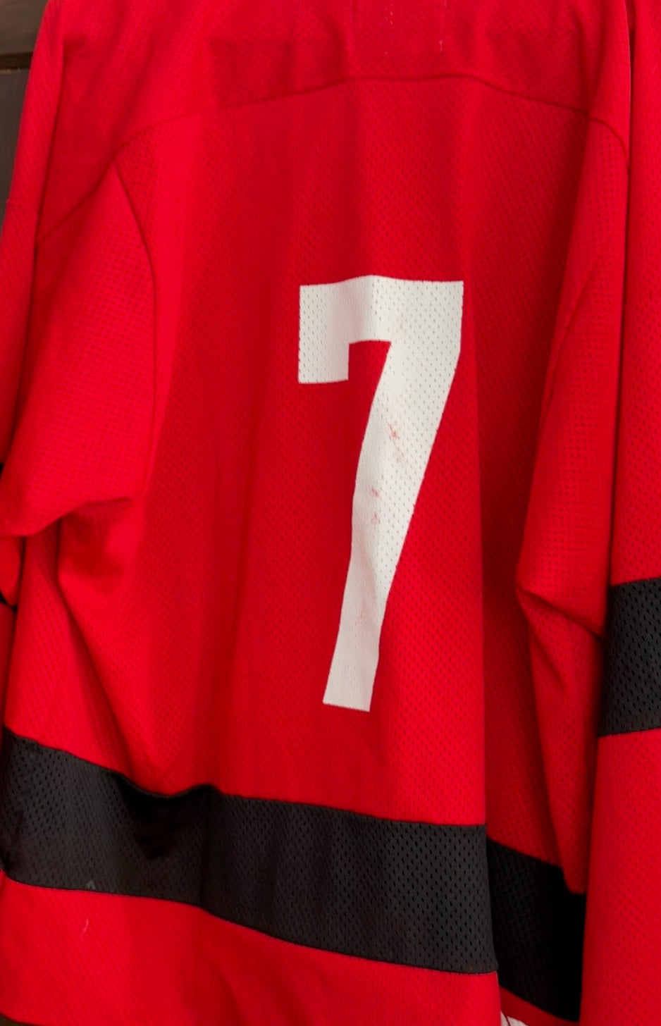 Red sports jersey with number 7 hanging on a wooden door.