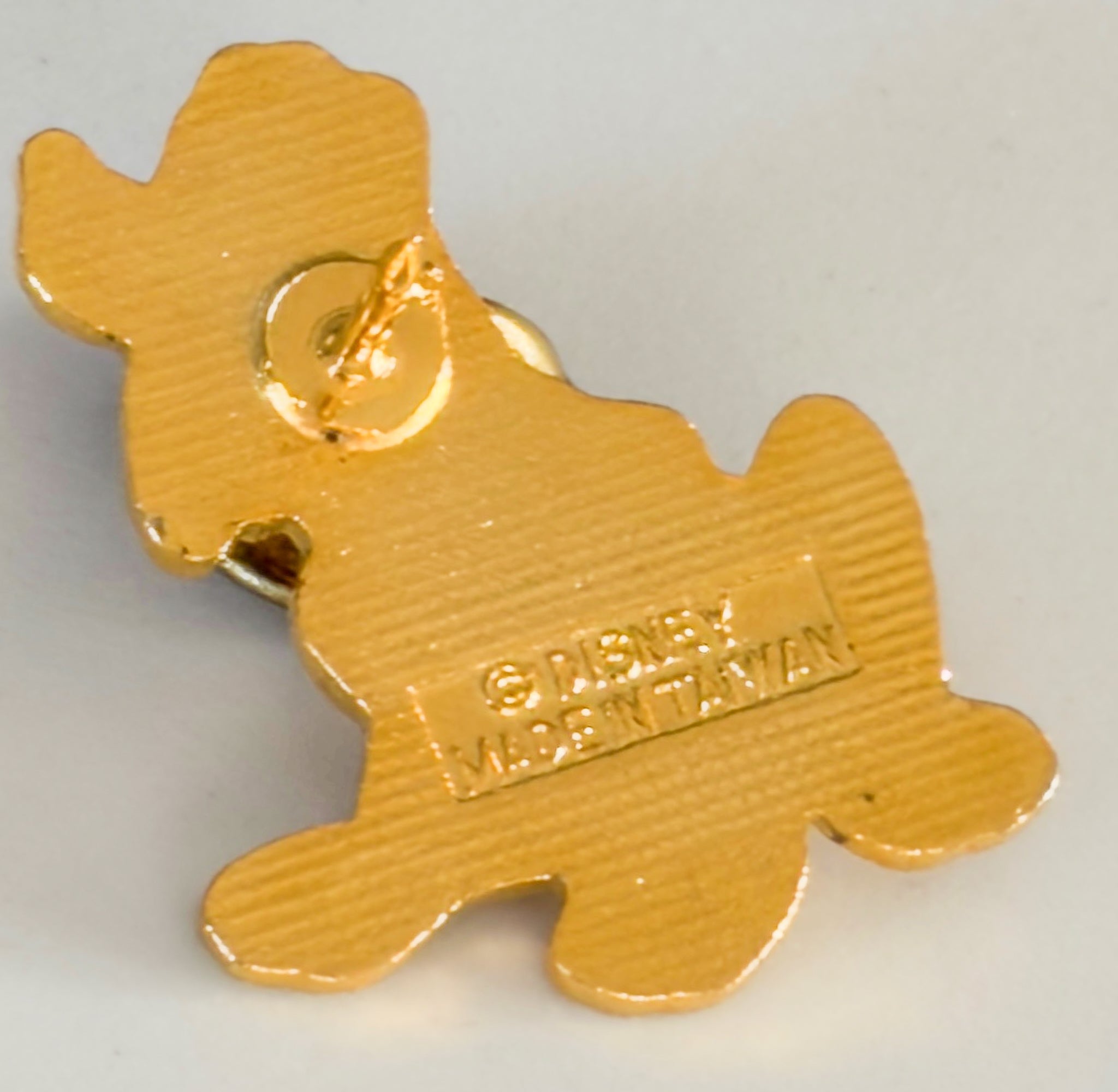Gold-colored keychain shaped like a dog with 'Disney' branding on a light gray background