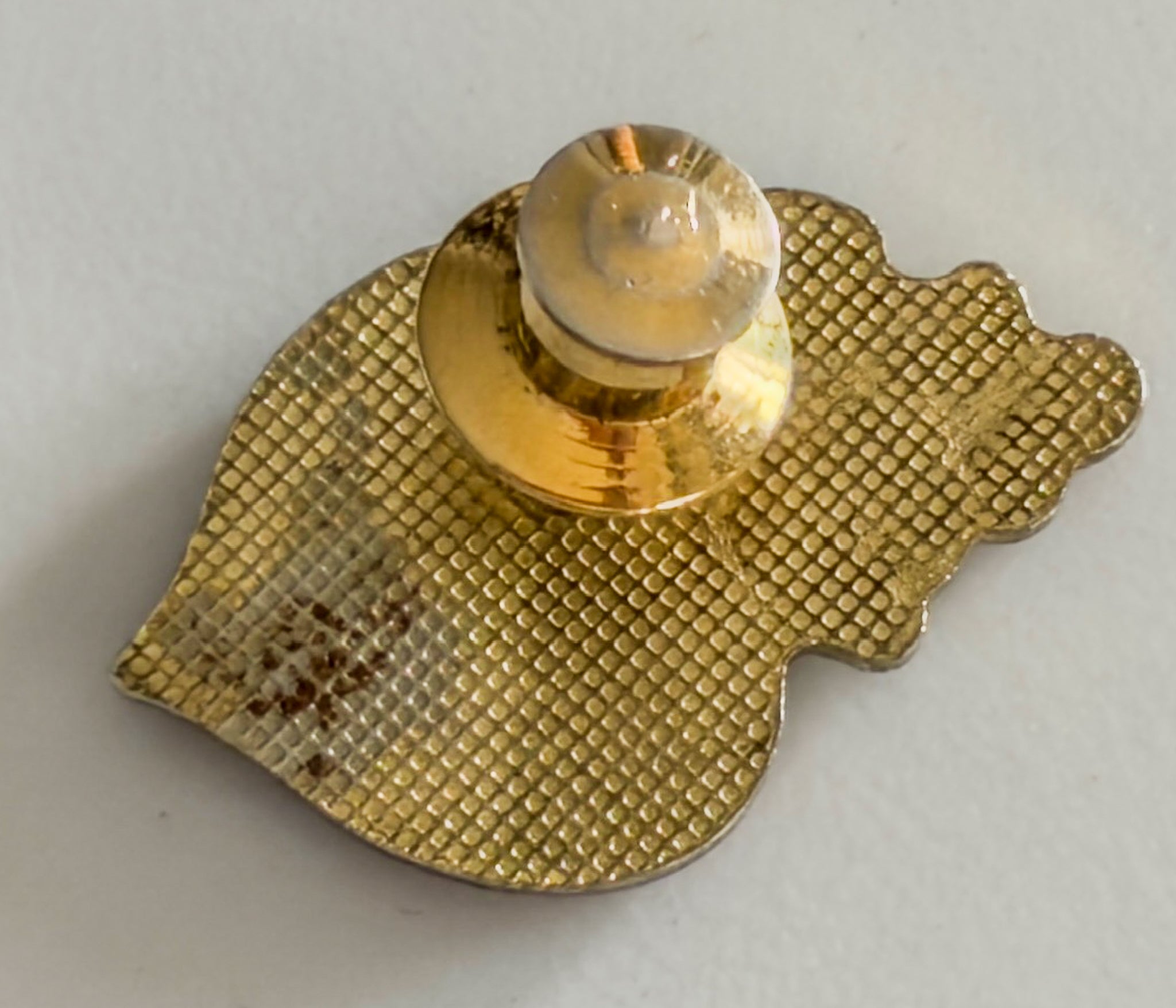 Gold-colored earring with textured design on a light gray background