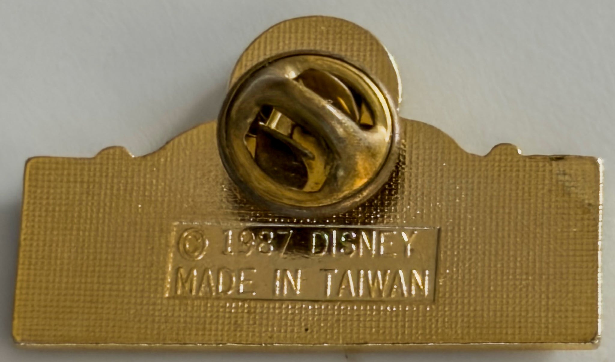 Gold Disney pin with 'Made in Taiwan' text on a gray background