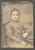 Vintage photograph of a young boy in a plaid outfit sitting on a chair.