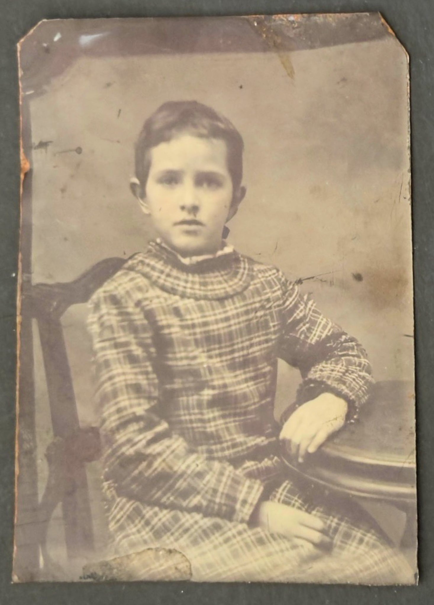 Vintage photograph of a young boy in a plaid outfit sitting on a chair.