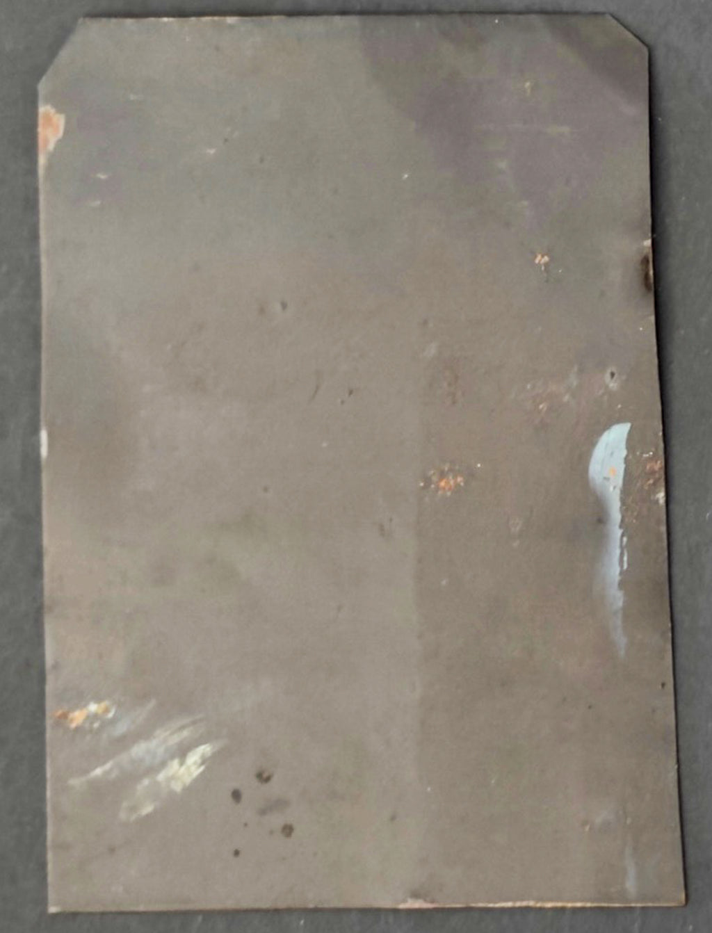 Metallic sheet with visible rust and discoloration on a dark background