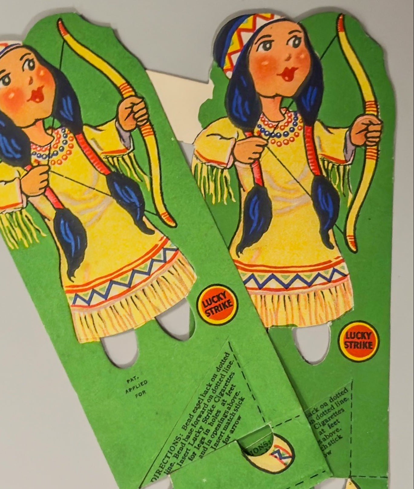 Vintage die-cut of an Native American woman with a bow and arrow on green paper.