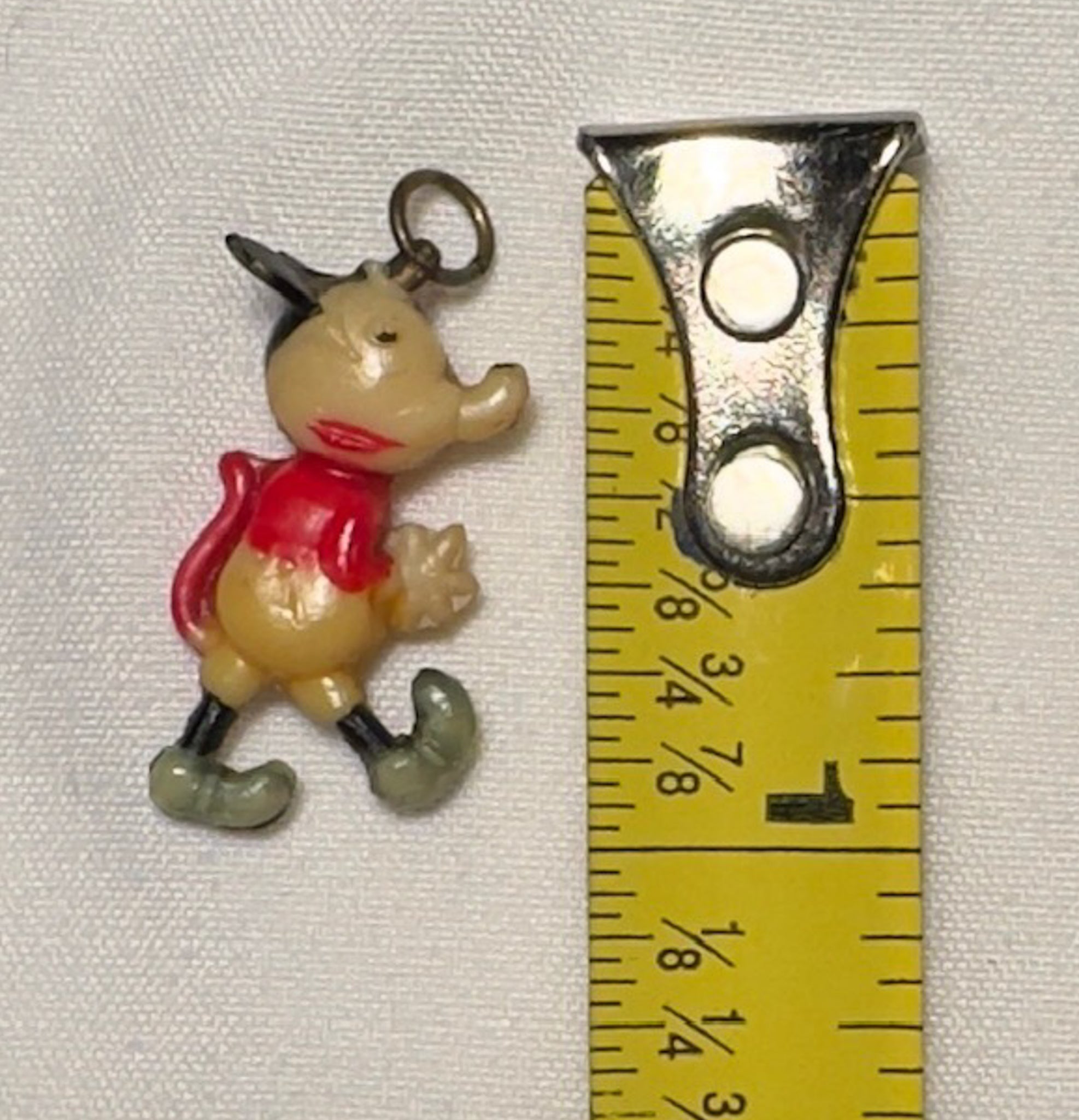 Small cartoon character charm next to a ruler on a white background