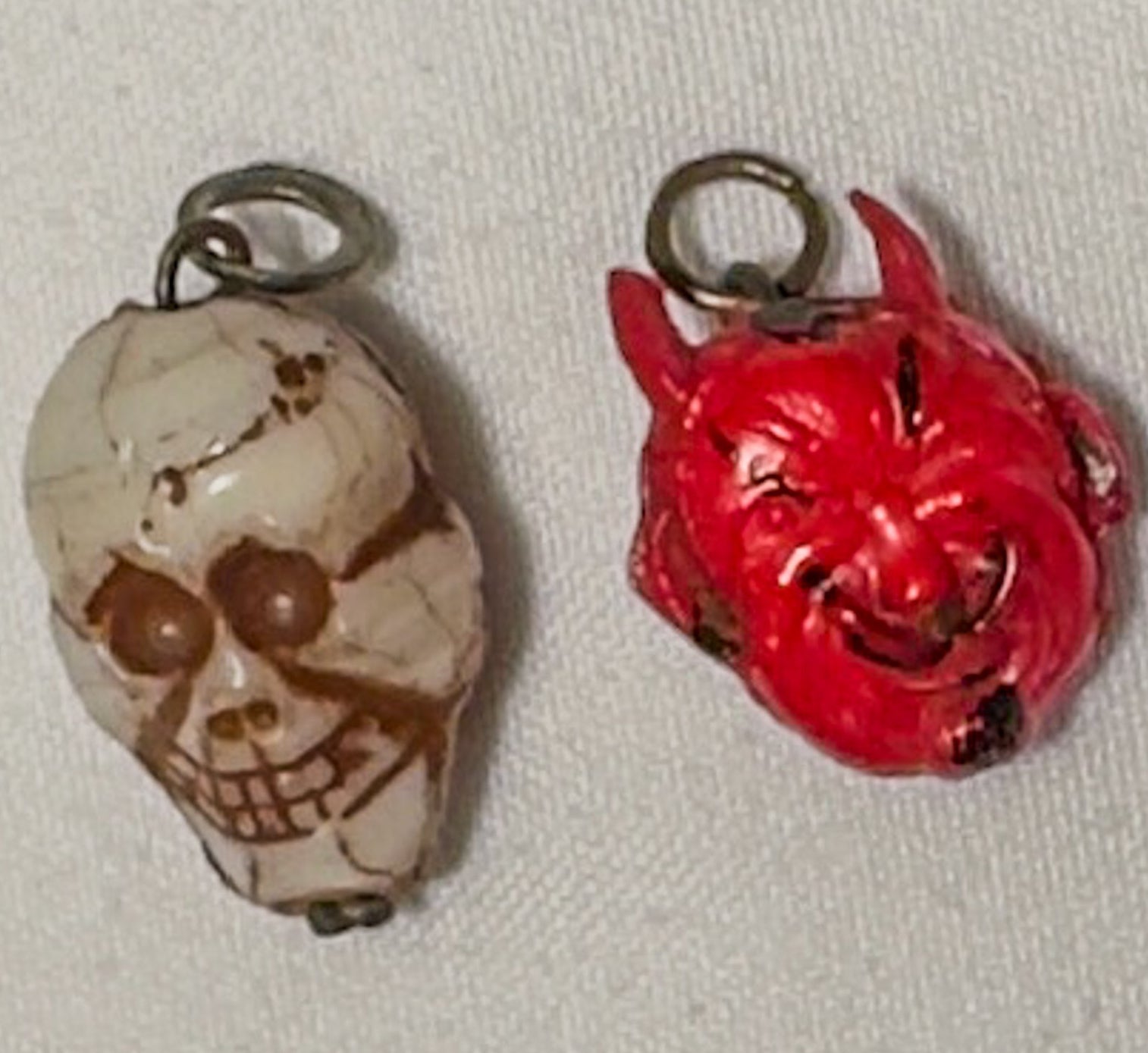 Two pendants, one skull-shaped and one red devil-like figure, on a light gray background.