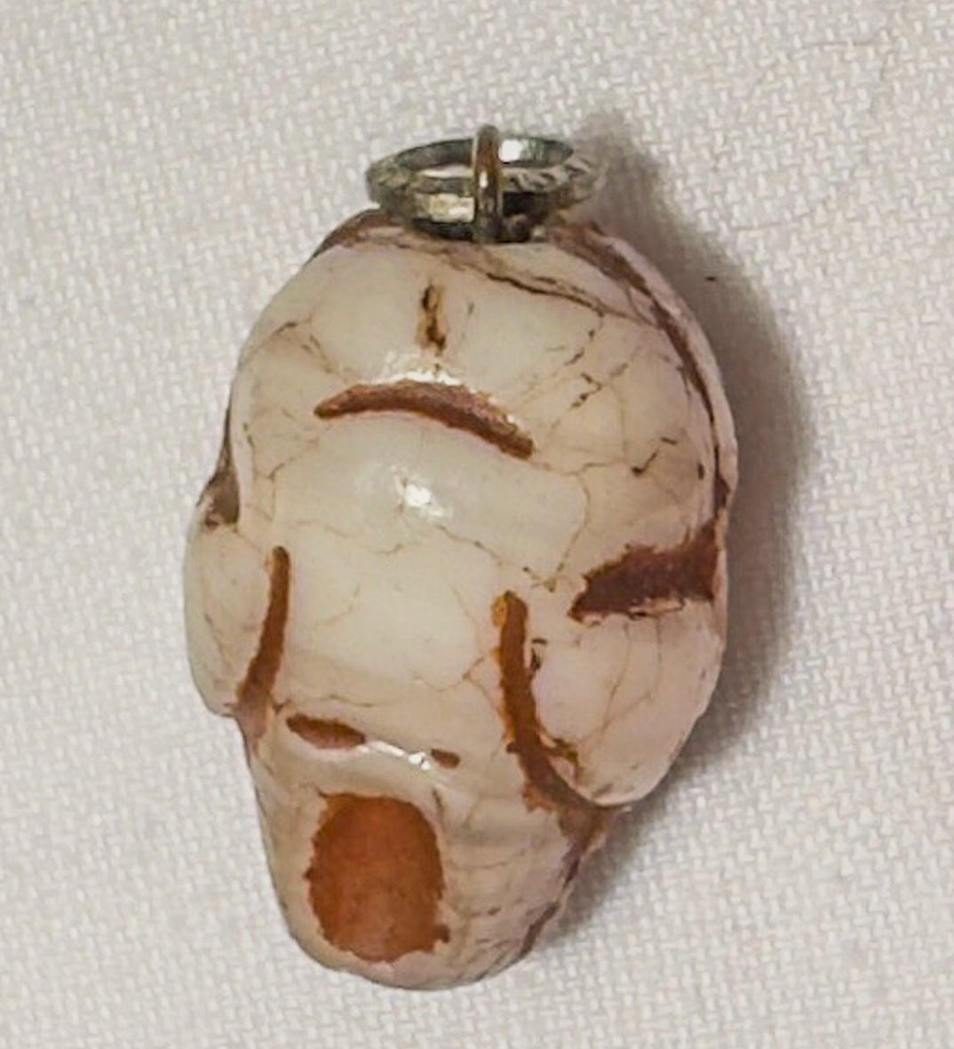 Two pendants, one resembling a skull and the other a red devil face, on a light fabric background.